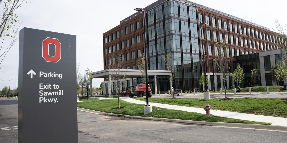 An exterior view of the building where a way finding sign is seen in the forefront.