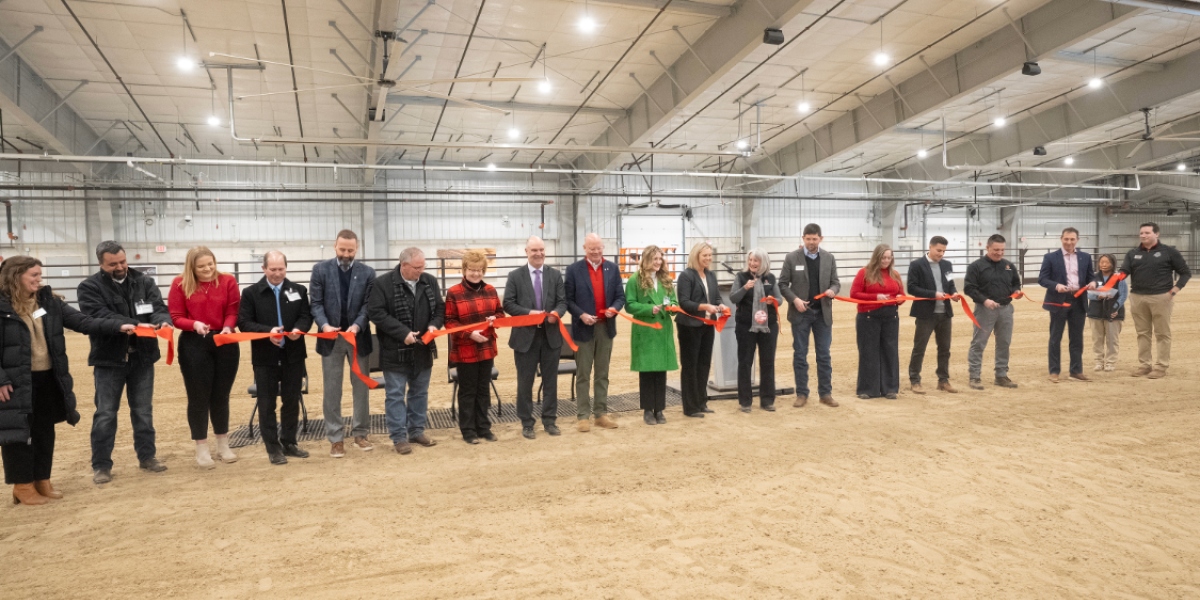 Several people are seen holding a red ribbon ready to cut it together.