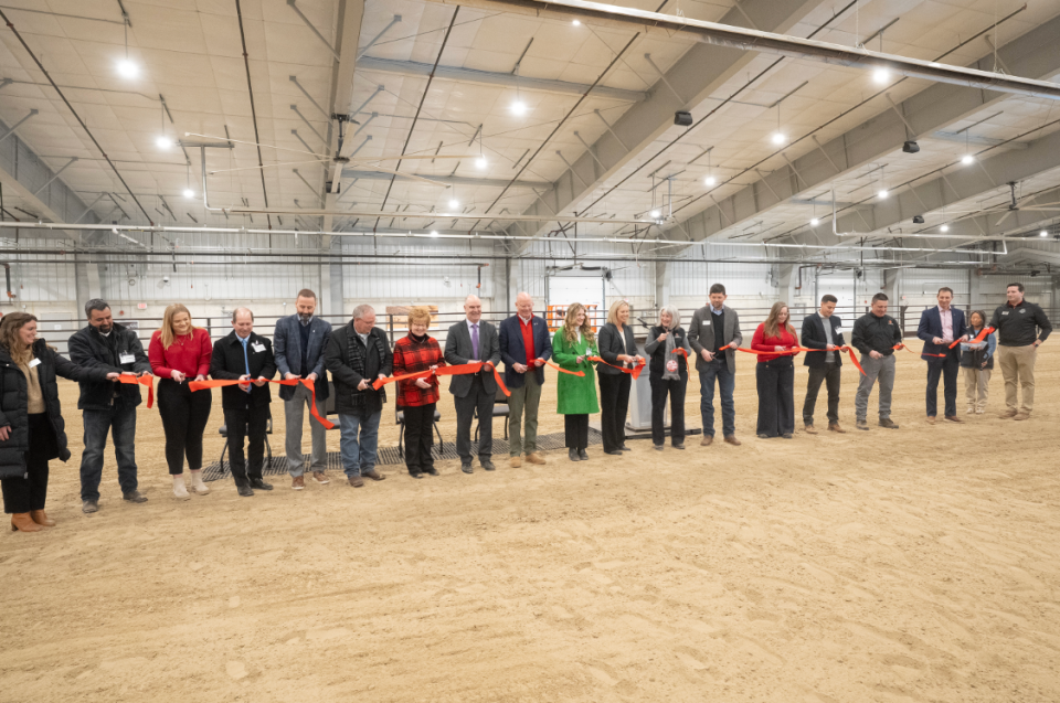 Several people are seen holding a red ribbon ready to cut it together.